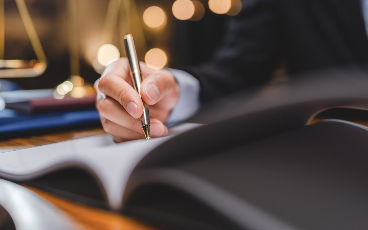 a business man's hand sgining a document with a silver pen.