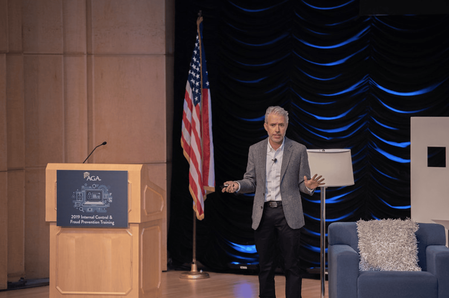 A man stands on stage at Fraud 2019 addressing the crowd from the side of the podium