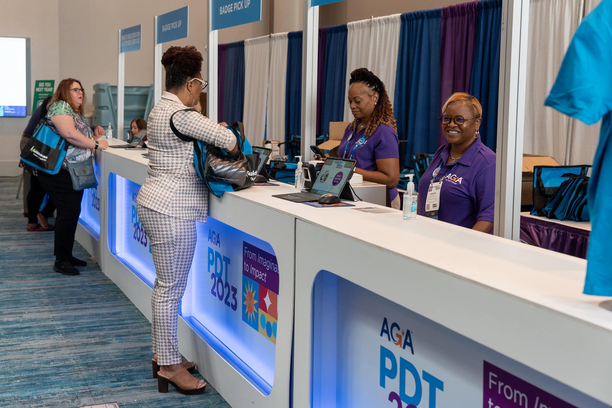 Two female AGA volunteers assisting PDT '23 attendees at the registration desk