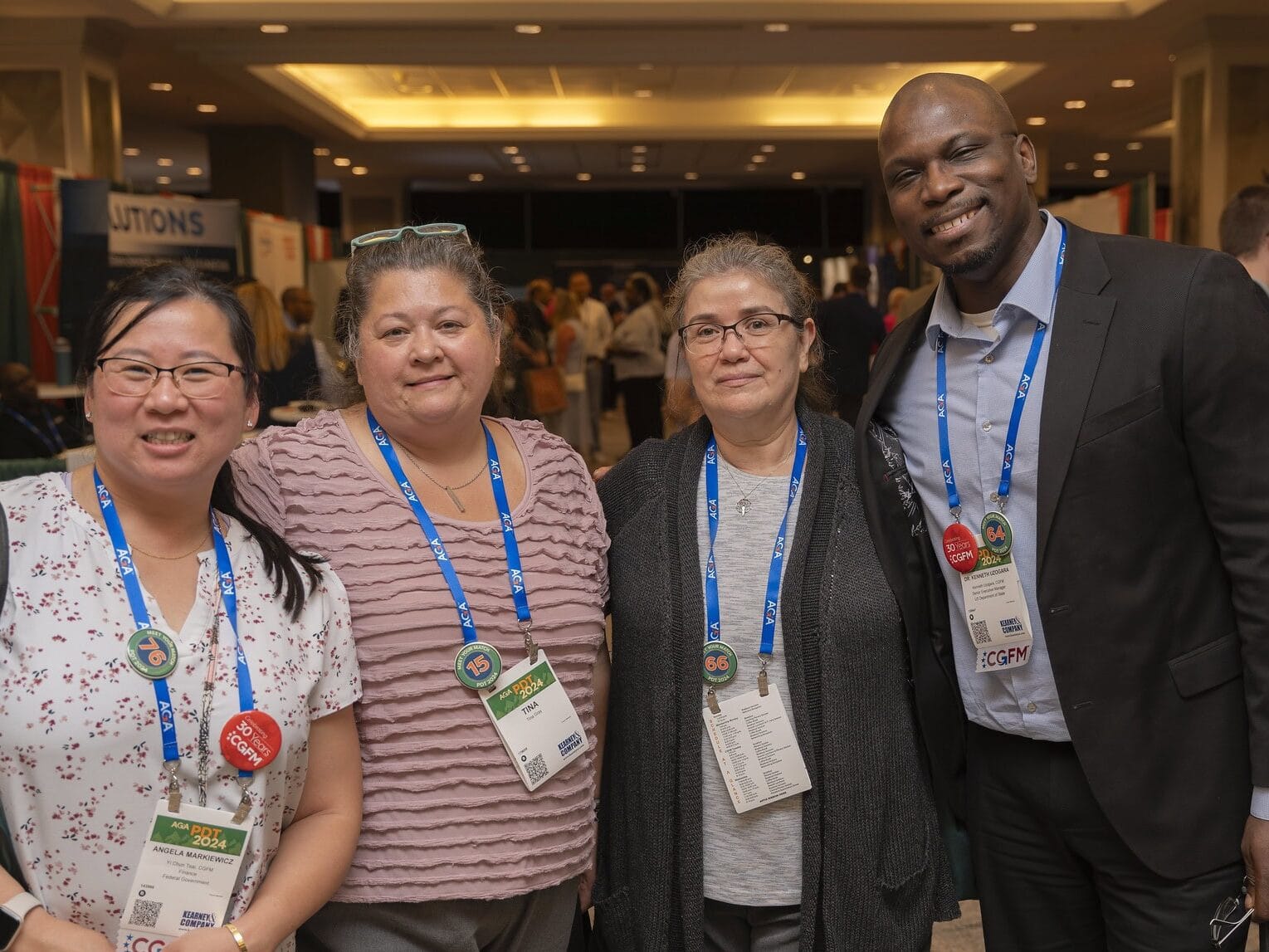 A group of four AGA event attendees stand shoulder-to-shoulder, excited to be in the Solutions Hall at PDT