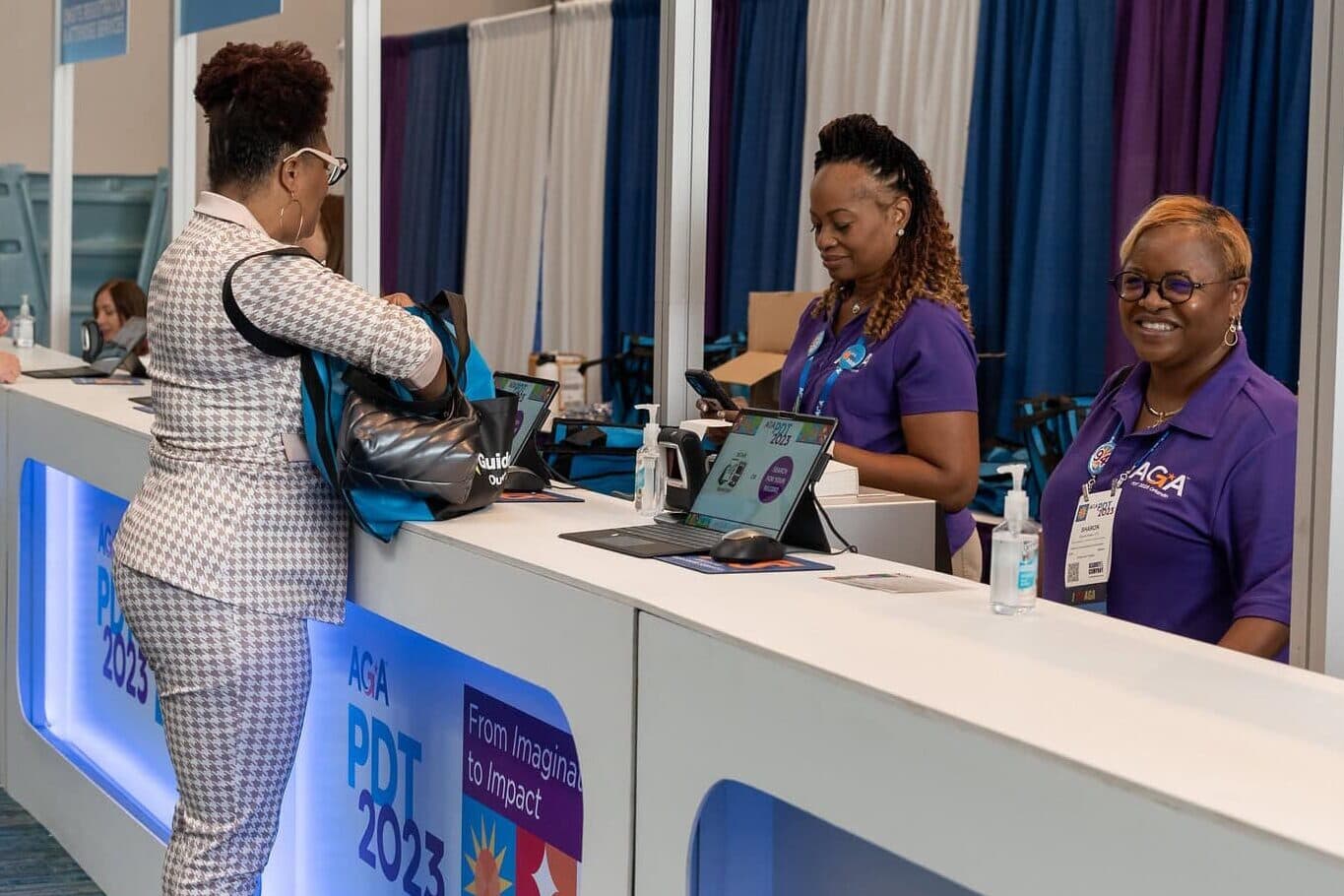 Two female AGA volunteers assisting PDT '23 attendees at the registration desk